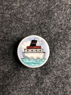 a button with a boat on it sitting on top of a carpeted floor next to a wall