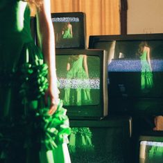 a woman in a green dress standing next to televisions with their reflection on them