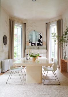 a dining room table and chairs in front of two large windows with curtains on them