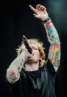 a black and white photo of a man with tattoos on his arms holding a microphone