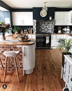 a kitchen with wooden floors and white cabinets is pictured in this image, there are two stools at the center of the island