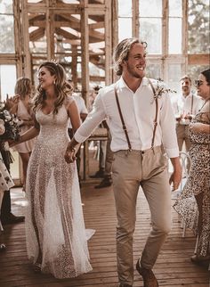 a man and woman holding hands walking down a wooden floor with other people in the background