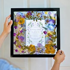 a person holding up a frame with flowers on it