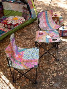 two lawn chairs sitting next to each other in front of a tent and picnic table