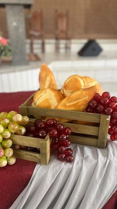 some bread and grapes are sitting on a red table cloth with white napkins in front of them