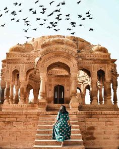 a woman standing on steps in front of a building with birds flying overhead