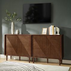 a tv mounted on the wall next to a wooden cabinet with books and vases