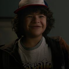 a young boy with curly hair wearing a red, white and blue hat smiling at the camera