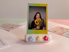 a photo frame with flowers on it sitting on a table next to cards and magnets