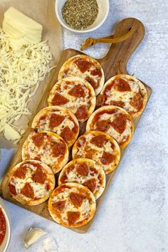 several small pizzas with cheese and sauce on a cutting board next to condiments