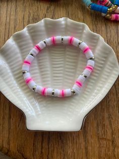 pink and white beaded bracelet sitting on top of a white shell shaped plate next to colorful beads