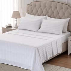 a bed with white sheets and pillows on top of it next to a night stand