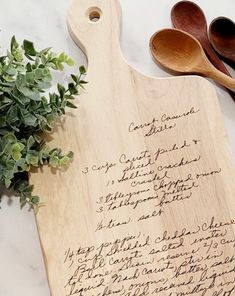 a cutting board with writing on it next to wooden spoons and plants in the background