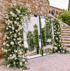 an outdoor ceremony setup with white flowers and greenery on the side of a stone building