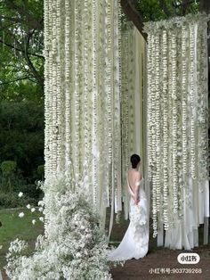 a woman standing in front of a white flower covered structure with flowers hanging from it's sides