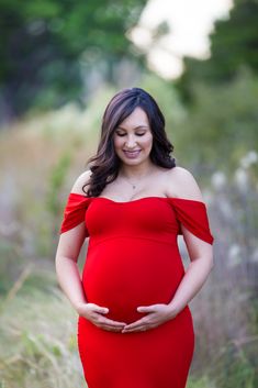 a pregnant woman in a red dress poses for the camera with her hands on her belly