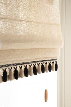 a white window with black tassels hanging from it's side and a curtain rod