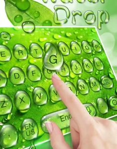 a hand is touching the keys on a green computer keyboard with water drops all over it