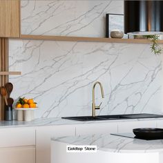 a kitchen with marble counter tops and white cabinets, along with black hanging lights above the sink