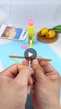 someone is making a paper airplane on a table with other items around it and one hand holding a piece of wood