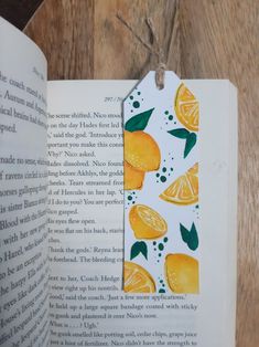 an open book with oranges and leaves on the pages, hanging from a string