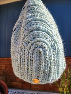 a blue knitted object hanging from a hook on a wall next to a potted plant