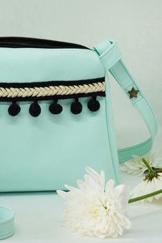 a white flower sitting next to a light blue purse with tassels on it