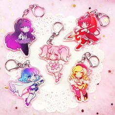 six anime keychains on a doily with stars and glitters in the background