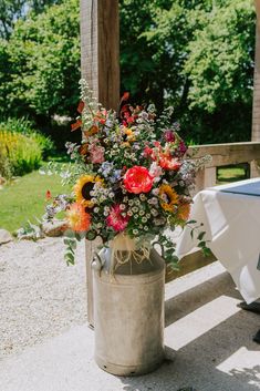 a vase filled with lots of flowers sitting on top of a wooden bench next to a white table cloth