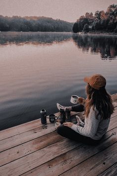 a woman sitting on a dock next to a lake