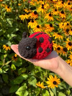 a ladybug stuffed animal sitting on top of a person's hand in front of flowers