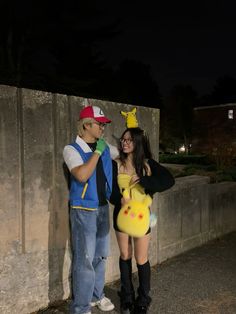 two people dressed up as pokemon and pikachu standing next to each other in front of a stone wall