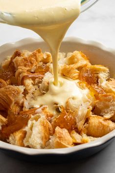 a bowl filled with bread and pudding being drizzled with cream on top