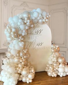 an arch made out of balloons and white flowers on a wooden table in front of a sign