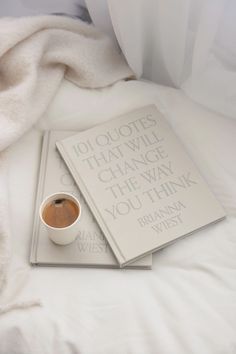 there is a cup of coffee next to two books on a bed with white sheets