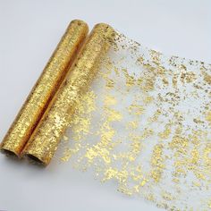 two rolled up gold glitter paper next to each other on a white surface with golden foil sprinkles