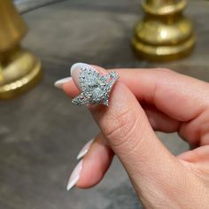 a woman's hand holding a diamond ring in front of her face, with gold and white decorations on it