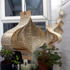 three paper lanterns hanging from a string with plants in front of them on the side of a building