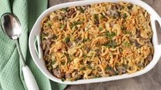 a casserole dish with meat and vegetables in it on a green napkin next to two spoons