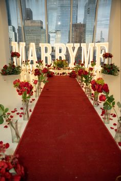 a long red carpeted aisle with flowers and candles on it in front of large windows