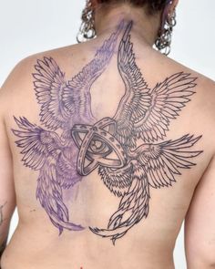 the back of a woman's tattoo with two birds on her shoulder and an eye in the center