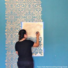 a woman is painting on the wall with blue and white stencileds in front of her