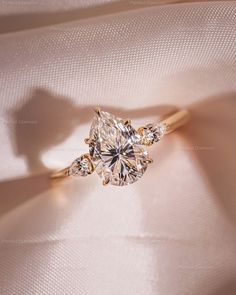 an engagement ring with three pear shaped diamonds on the top and bottom, sitting on a white cloth