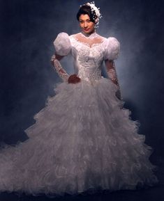 a woman in a white wedding dress with long sleeves and ruffles on the skirt