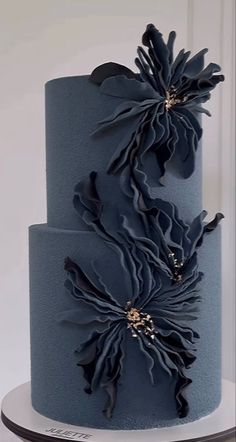 a three tiered blue cake with large flowers on it's top and sides