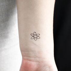 a small tattoo on the wrist of a woman's left arm with an atomic symbol