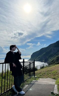 a man sitting on top of a metal rail next to a lush green hillside under a blue sky