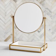 a round mirror sitting on top of a white counter next to a gold frame and marble wall