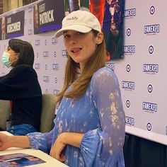 a woman sitting at a table in front of a poster