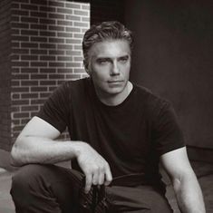 a black and white photo of a man sitting on the ground with his hand in his pocket